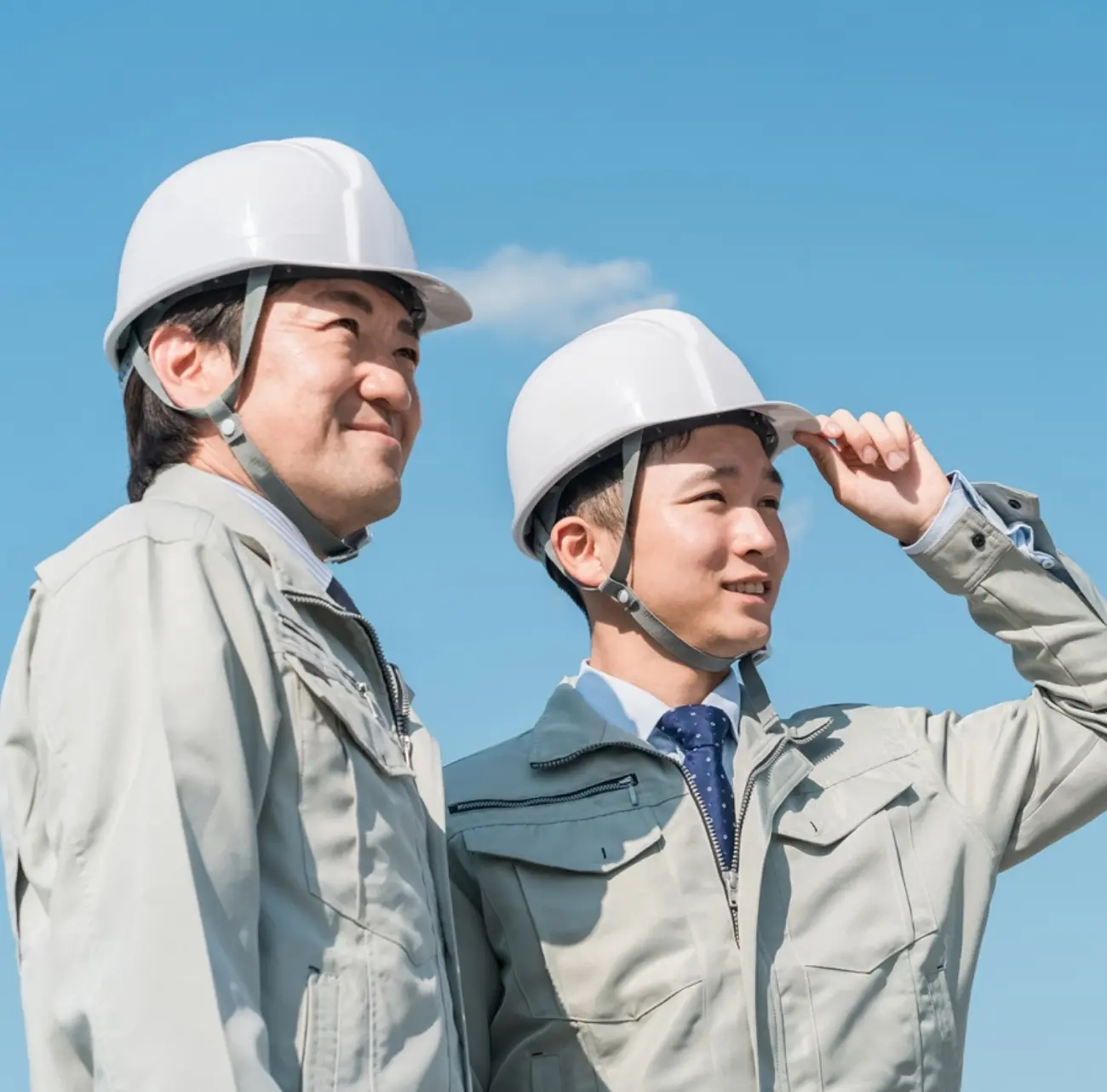 ヘルメットと作業着姿で空を見上げる若手社員達